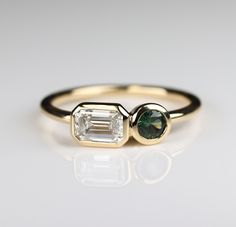 an emerald and diamond ring on a white surface