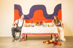 a man and woman sitting at a table in front of a large banner with wine bottles on it