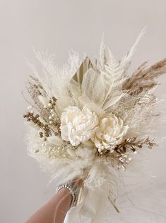 a hand holding a bouquet with flowers and feathers