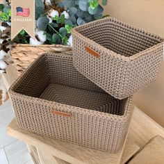 two woven storage baskets sitting on top of a wooden table next to a planter