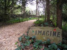 a sign that is sitting in the grass near some trees and leaves on the ground