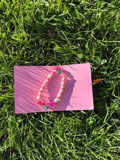 a bracelet laying on top of a pink piece of paper in the middle of grass