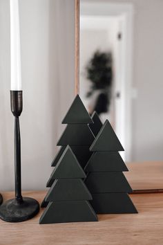 three small christmas trees sitting on top of a wooden table next to a white candle