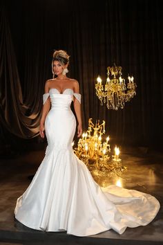 a woman in a white wedding dress standing next to a chandelier with candles