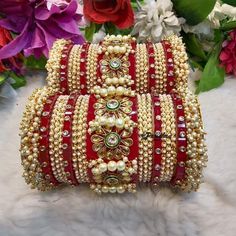 three red and gold bangles with pearls on them, sitting next to some flowers