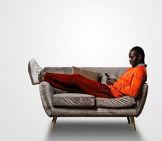 a man in an orange shirt is sitting on a couch with his legs crossed and holding a cell phone