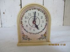 an antique clock with floral designs on it's face is displayed in front of a white wooden wall