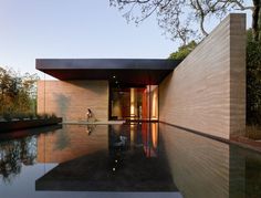 a person sitting on the edge of a swimming pool in front of a house with trees