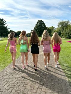 four women in short dresses walking down a path with their backs turned to the camera