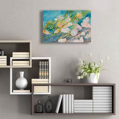 a shelf with books and vases on top of it next to a wall mounted painting