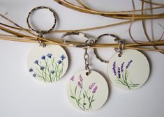 three keychains with flowers painted on them sitting next to some twigs and twig