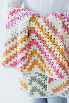 a woman is holding a crocheted blanket in her hands