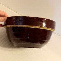 a hand holding a brown bowl on top of a white table