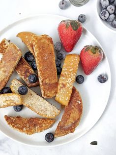 a white plate topped with french toast and blueberries next to strawberries on a table