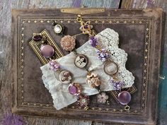 an old suitcase with buttons and lace on it sitting on a wooden table next to other items