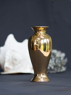 a gold vase sitting on top of a table next to a white flower pot and seashell