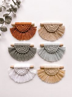 four different colored tassels hanging on a wall next to eucalyptus branches and flowers