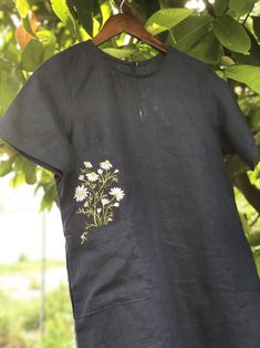 a t - shirt hanging from a tree with daisies in the pocket on it