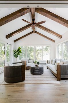 a living room with white couches and wooden beams on the ceiling is filled with windows