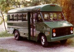 an old green bus is parked on the side of the road in front of some trees