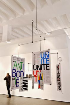 a person standing in an art gallery looking at posters hanging from the ceiling above them