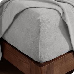 a bed with a wooden headboard and foot board on top of it, covered in a light gray blanket