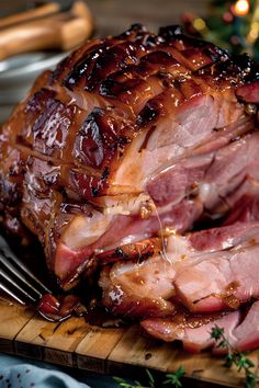 sliced ham on a wooden cutting board with fork and knife next to christmas tree in background