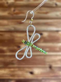 a pair of dragonfly earrings hanging from a hook on a wooden background with beads