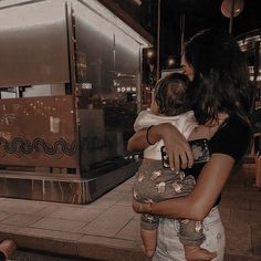 a woman holding a baby in her arms on the sidewalk at night time with people walking by