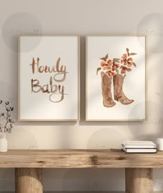 two framed art prints with flowers and cowboy boots are on the wall next to a wooden table