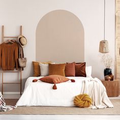 a white bed topped with lots of pillows next to a wooden shelf filled with blankets