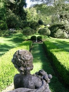 a stone statue sitting in the middle of a lush green park filled with trees and bushes