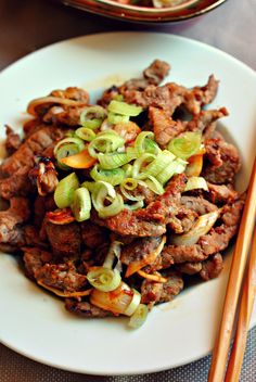 a white plate topped with meat and vegetables next to chopsticks