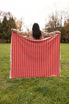 a woman standing in the grass with her back to the camera holding up a red and white blanket