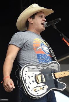 a man in a cowboy hat singing into a microphone and playing an electric guitar on stage