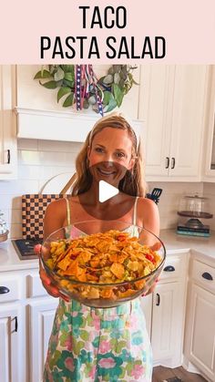 a woman standing in a kitchen holding a bowl of food with the words taco pasta on it