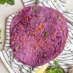 a purple tortilla sitting on top of a white and black towel next to a bowl of guacamole