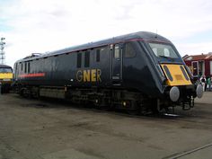 a black and yellow train is parked on the tracks next to some people standing around