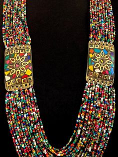 This is a wonderful colorful vintage Naga necklace with two mosaic inlay brass medallions that also serve as connectors for the multi bead strands.  There are 21 strands connected to the top of the mosaic medallion, and 24 rows connected to the bottom of the medallions.   The medallions have a decorative brass sun at center, with their rays having scalloped edges, and a tiny beaded effect frames the center brass circle. The inner circumference of the necklace measures approximately 31". Fastens with a blue disc bead and loop.  Medallions measure approximately 2-1/4" X 1-3/8" Excellent vintage condition.  No issues. Includes gift box and storage pouch. Box 1 Bohemian Multicolor Brass Necklace, Bohemian Multicolor Brass Necklaces, Traditional Multicolor Jewelry With Gold Beads, Festival Gold Beads, Traditional Multicolor Medallion Beaded Necklaces, Traditional Multicolor Medallion Beaded Necklace, Traditional Medallion Beaded Necklaces In Multicolor, Multicolor Round Beads Brass Necklace, Multicolor Round Bead Brass Necklace