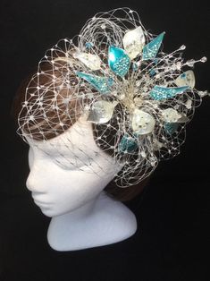 Teal blue and silver veiled fascinator perfect for the guest who wants something beautifully unique. This design is a beautiful selection of glass effect leaves and flowers clustered together amongst a fine layer of veiling and set onto a fine comfort base tiara band. As with all our designs, this piece can be made exact to the image or in any colour combination to match in with your outfit. If a specific colour is required customers can message over an image of their outfit and accessories, or Silver Headpiece For Party At Royal Ascot, Silver Headpieces For Party At Royal Ascot, Silver Headpiece For Evening At Royal Ascot, Silver Evening Headpiece For Royal Ascot, Silver Headband Fascinator For Party, Handmade Silver Headpieces For Party, Silver Mini Hats For Royal Ascot Wedding, Silver Mini Hats For Wedding At Royal Ascot, Silver Fascinator For Wedding At Royal Ascot