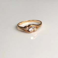 An vintage 9 carat gold ring displaying three diamonds. The three stones sit beautifully in an unusual setting. CONDITION: Wear consistent with age and use. Please see photos for more detail. HALLMARKED 9 CARAT GOLD, ASSAYED IN LONDON 1988 BAND WIDTH: 1.5mm DIAMOND SIZE:  3mm (0.10ct) 1.5mm (0.01ct) SETTING LENGTH: 20mm SETTING HEIGHT: 5mm RING SIZE: UK: M | US: 6 1/4 WEIGHT: 1.5g Small Vintage Ring, Heirloom Diamond Reset, Unique Bezel Set Engagement Ring, Gold Three Stone Art Deco Diamond Ring, Vintage Yellow Gold Three Stone Rings, Art Deco Gold Three Stone Diamond Ring, Art Deco Three Stone Gold Diamond Ring, Vintage 14k Gold Three-stone Rings, Vintage 14k Gold Three Stone Rings