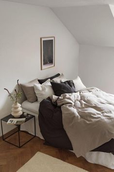 a bed sitting in a bedroom next to a white wall with a painting on it