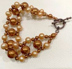 Copper and gold Swarovski crystal pearls of various sizes have been woven by hand into a luxurious bracelet fastened with a copper toggle clasp.  The bracelet is about 7 3/4 inches long.  Comes nestled on a bed of cotton in a white cardboard jewelry box.  NA-444-C30 Elegant Bronze Bracelets With Round Beads, Handmade Elegant Bronze Beaded Bracelets, Adjustable Gold Copper Bracelet, Elegant Bronze Beaded Bracelets, Elegant Brown Bracelet With Lobster Clasp, Elegant Gold-colored Copper Bracelets, Twisted Copper Wire Bracelet, Adjustable Wire-wrapped Copper Wire Bracelets, Luxury Gold-tone Brass Bracelet