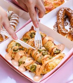 a person holding a fork in a box filled with pastries and pretzels