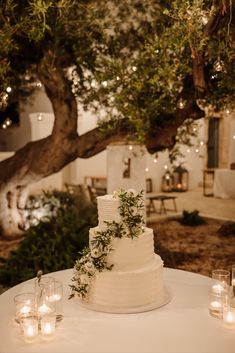 a white wedding cake sitting on top of a table next to candles and a tree