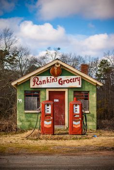 an old green building with two red gas pumps