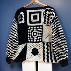 a black and white knitted sweater hanging on a coat hanger against a blue wall