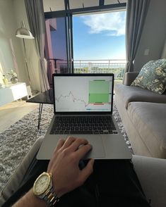 a man sitting in front of a laptop computer on top of a couch next to a window