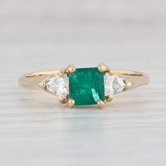 an emerald and diamond three stone ring on a wooden table with white wood flooring