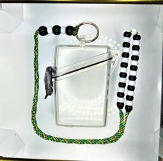 a white box with some black and green beads on it next to a keychain